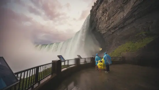 Menschen in blauen und gelben Regenmänteln schützen sich vor dem Nebel der Niagarafälle.
