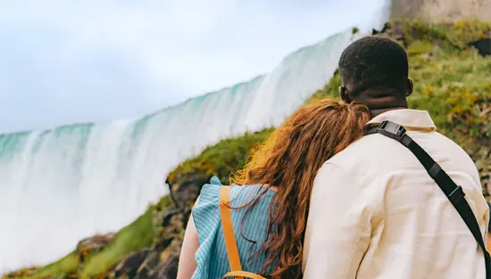 A couple standing close together in front of Niagara Falls, surrounded by other visitors in blue ponchos.
