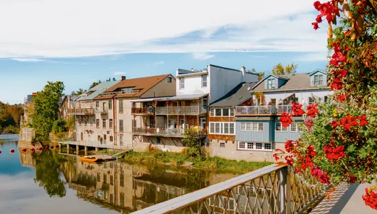 Des maisons sur le bord du lac à Elora qui se reflètent sur l’eau calme, encadrées par des fleurs d’un rouge éclatant.