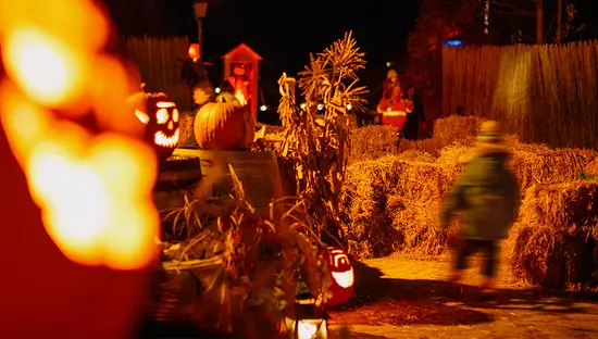 干し草の俵と光るカボチャが道を照らす不気味なハロウィーンの小道を子供が歩いています。
