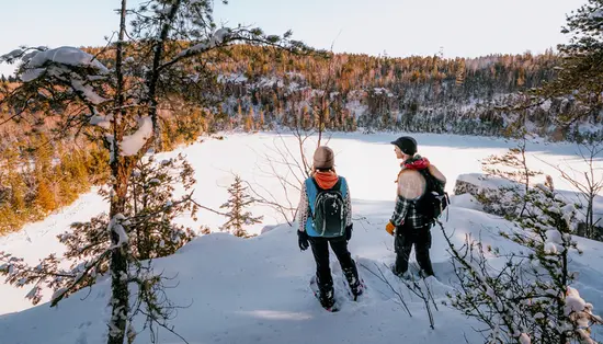 Zwei Schneeschuhwanderer in Nord-Ontario halten an, um den Blick auf den schneebedeckten Wald jenseits eines zugefrorenen Sees zu bewundern.