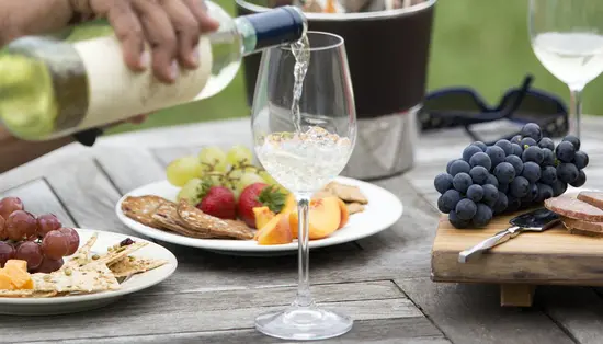 Une personne verse un verre de vin blanc pour accompagner des fruits et des fromages lors d’un pique-nique en plein air à l’établissement vinicole Viewpointe.