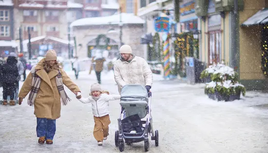 Parents hold the hands of their young daughter as the happy family strolls along a snowy sidewalk during the holiday season.