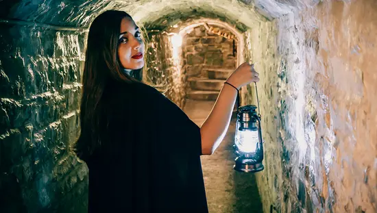 A woman leads a haunted walk, glancing over her shoulder as she enters a dark tunnel.