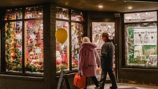 A couple walks past the windows of a store lit up at night and decorated for the holidays.