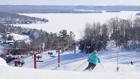 青い冬用コートを着たアルペンスキーヤーが、マスコーカのヒドゥンバレーにあるスキーコースを滑降している。