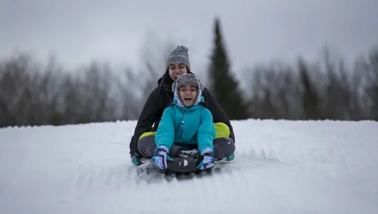한 십대 소녀와 한 젊은 여성이 머스코카의 겨울 리조트에서 썰매를 타고 눈 덮인 언덕을 내려가고 있습니다.
