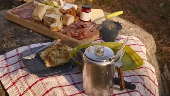 広大な湖を見下ろすキャンプ場で、カップルが燃え盛る火の前の丸太のベンチに座っている。