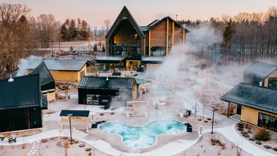  晩秋の木々に囲まれた屋外ノルディック スパの温水プール、冷水プール、サウナ、スチーム ルームからは蒸気が立ち上っています。