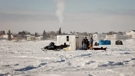 Ice anglers stand beside a snowmobile and an ice fishing hut on a frozen lake during the Wawa Ice Fishing Derby.