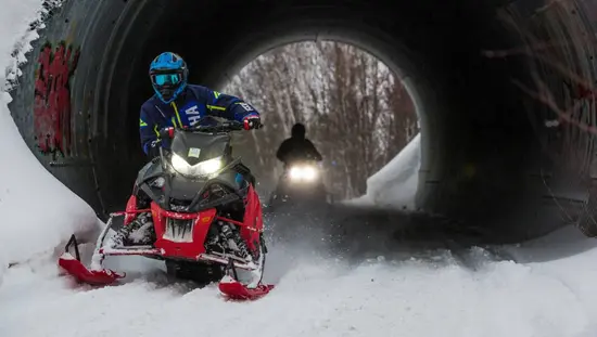 Two snowmobilers ride along a trail through a tunnel on a guided snowmobile trip in Sudbury.