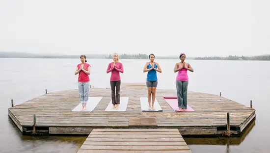 Group of people meditating on a wooden dock overlooking a calm lake.