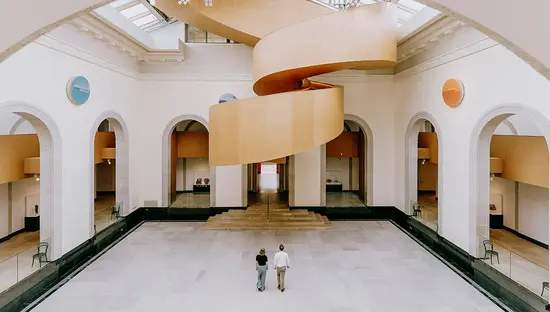 Spacious museum atrium with curved balconies and visitors walking across an open floor.