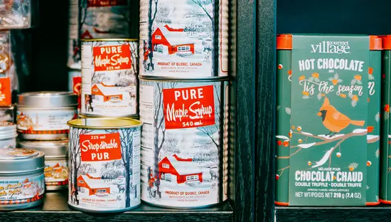 Cans of maple syrup and packaged chocolates displayed on shelves in a specialty food shop.