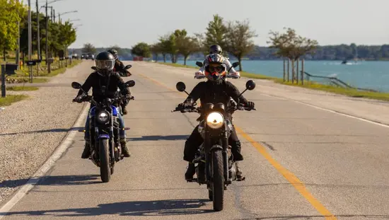A group of four motorcyclists rides a waterfront stretch of road on a summer day in Southwest Ontario.