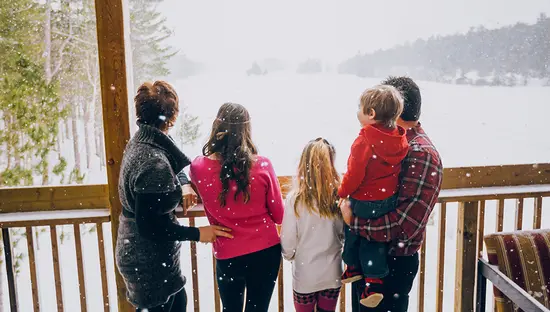 A family of five stands on a snowy balcony, looking out over a snow-covered forested landscape.