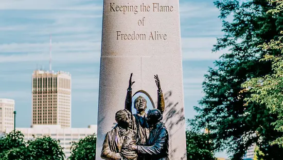 The Tower of Freedom monument in Windsor with sculpted figures and a city skyline in the background.