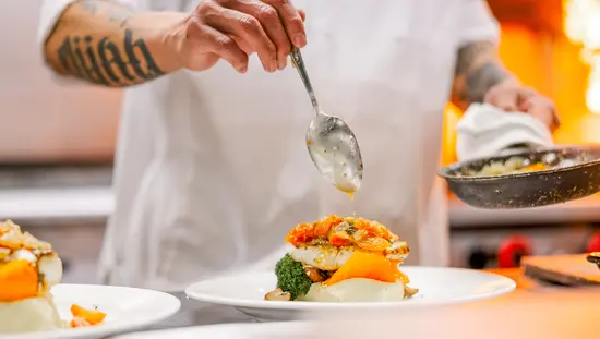 레스토랑 주방에서 요리사가 해산물 요리에 야채와 소스를 곁들여 접시에 담고 있다.