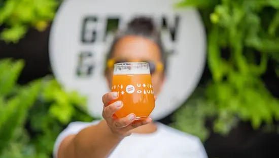 Eine Frau hält ein frisch gezapftes Glas Craft-Bier hoch und steht vor dem Brauereischild.