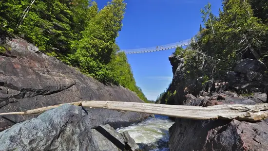 Des randonneurs traversent une passerelle suspendue au-dessus d'un torrent impétueux, le long d'un sentier de randonnée dans le parc national de Pukaskwa.