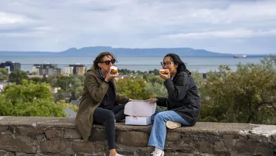 썬더베이에서 두 여성이 페르시아식 페이스트리를 즐기고 있으며, 배경에는 슬리핑 자이언트 산이 보인다.