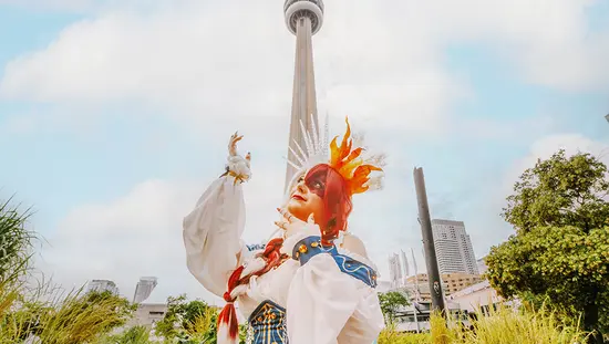 A person in elaborate cosplay is posing outdoors with the CN Tower in the background.