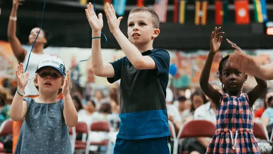 Kleine Kinder klatschen bei einer musikalischen Aktivität im Kinderbereich eines Kulturfestivals.