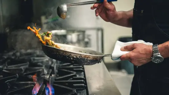Un chef est en train de faire frire des aliments à la poêle sur une flamme nue dans le restaurant Craft Farmacy.
