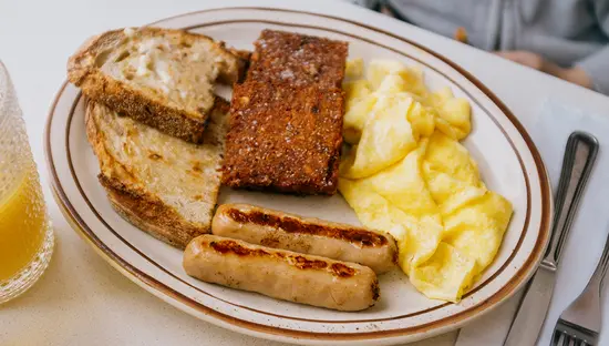Plato de brunch con huevos revueltos, salchichas, tostadas y un vaso de zumo de naranja.