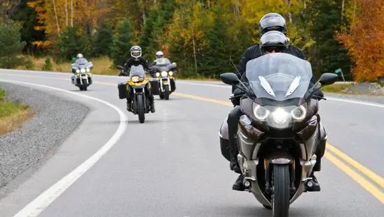 Un groupe de quatre motocyclistes emprunte une route asphaltée qui serpente à travers des forêts aux couleurs flamboyantes de l'automne à Muskoka.