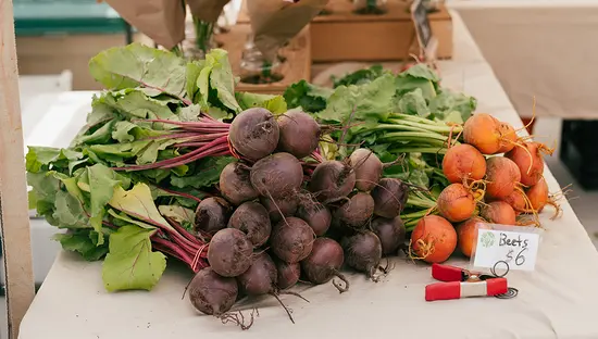 Betteraves et légumes frais étalés sur une table dans un marché fermier, avec des fleurs en arrière-plan.