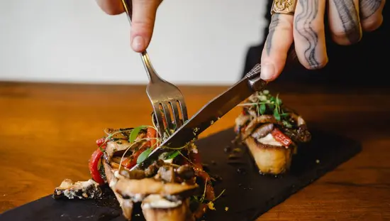 キングストンのレストランで、ある人がフォークとナイフを使って、美しく盛り付けられた前菜料理を切り分けている。