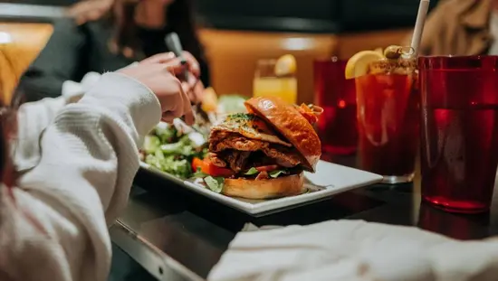Un hamburger juteux garni de nombreux ingrédients supplémentaires, servi avec une salade et une boisson fruitée.