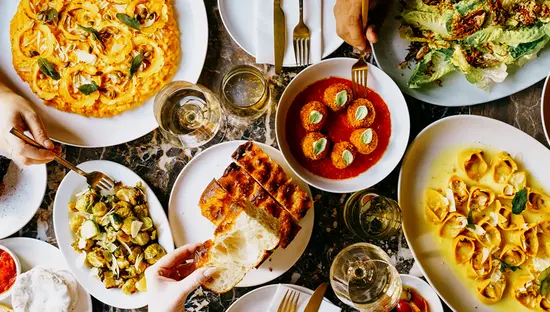 パスタ、リゾット、サラダ、パンなど、ヴィーガン料理のシェアプレートが並んだテーブルを上から見た写真。人々が手を伸ばして食べている様子が写っている。