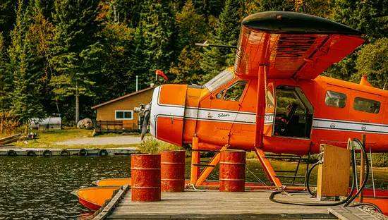 Floatplane parked at a wooden dock on a lake surrounded by forest.