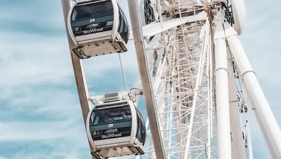 Grande roue blanche géante tournant lentement tandis que deux personnes dans une cabine admirent le paysage.