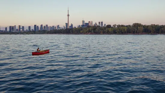 Un hombre lanzaba su caña de pescar desde una canoa en las aguas del puerto de Toronto, con la Torre CN y el perfil urbano de la ciudad de fondo.