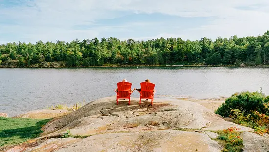 Deux chaises rouges sur une rive rocheuse surplombant un lac paisible entouré de forêt.