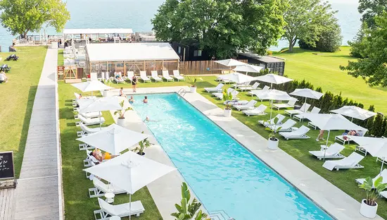Outdoor pool with lounge chairs and umbrellas at Lakeside Motel in Prince Edward County overlooking the water.