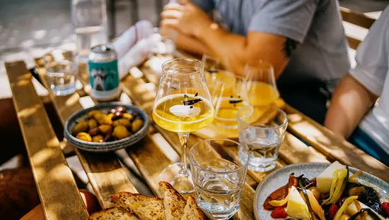 Verres de vin, petites assiettes et pain disposés sur une table de terrasse au soleil.