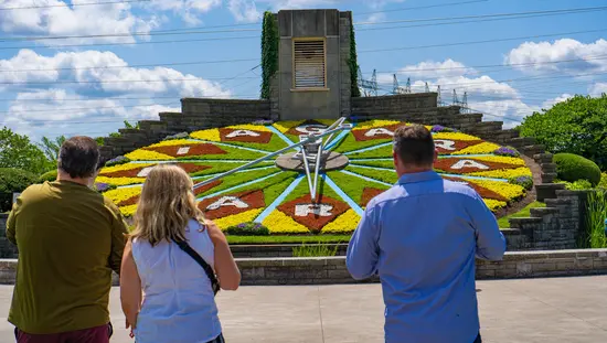 Three visitors viewing the Niagara Floral Clock, a large working clock face made of colorful flowers spelling 'Niagara Falls.