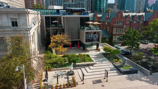 Aerial view of the Gardiner Museum in Toronto, featuring a modern building with rooftop terrace, landscaped courtyard, and outdoor sculptures, surrounded by the city skyline.