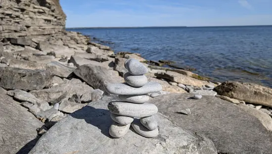 Stacked stone inukshuk on a rocky shoreline overlooking blue water and a limestone bluff.