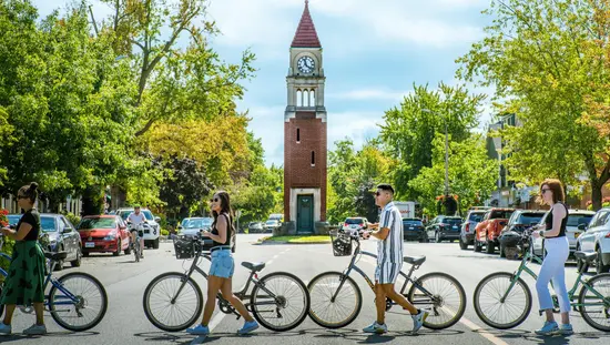 Four people with bicycles crossing the street in front of the clock tower.