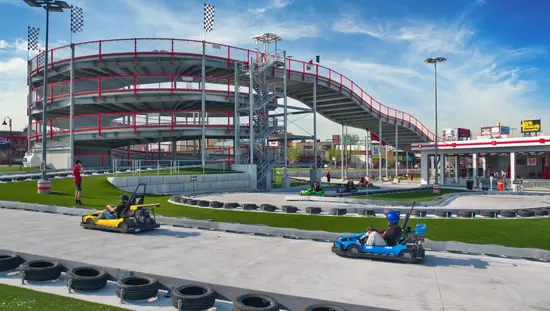 Multi-level go-kart track with a spiral ramp structure, checkered flags, and colorful karts racing on a concrete course.