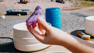 Someone holding a puple and blue amethyst at the beach. 