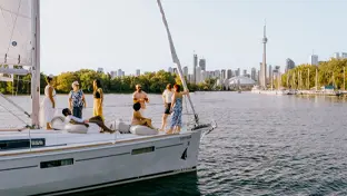 Groupe de personnes en train de socialiser sur un voilier naviguant sur l’eau, avec le centre-ville de Toronto et la Tour CN en arrière-plan.
