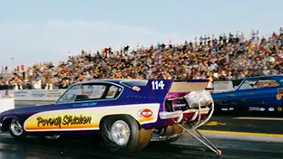A large crowd of fans watch cars race at the Grand Bend Motorplex.