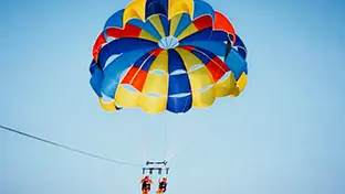 Two people gliding with a red, blue and yellow parasail in the clear sky.
