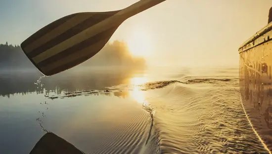 Un remo de canoa avanza suavemente por el agua hacia la puesta de sol.